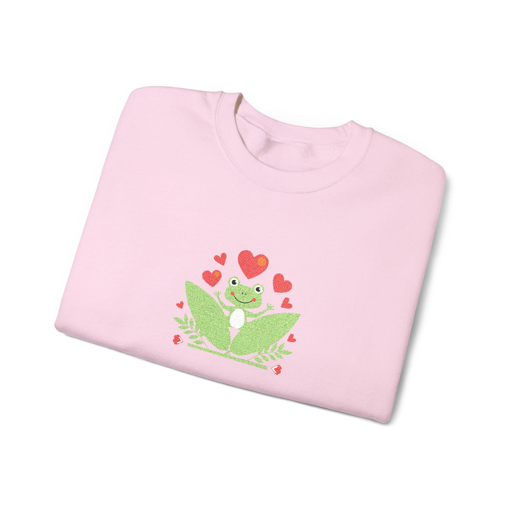Folded pink shirt with a green frog and red heart design on a white background