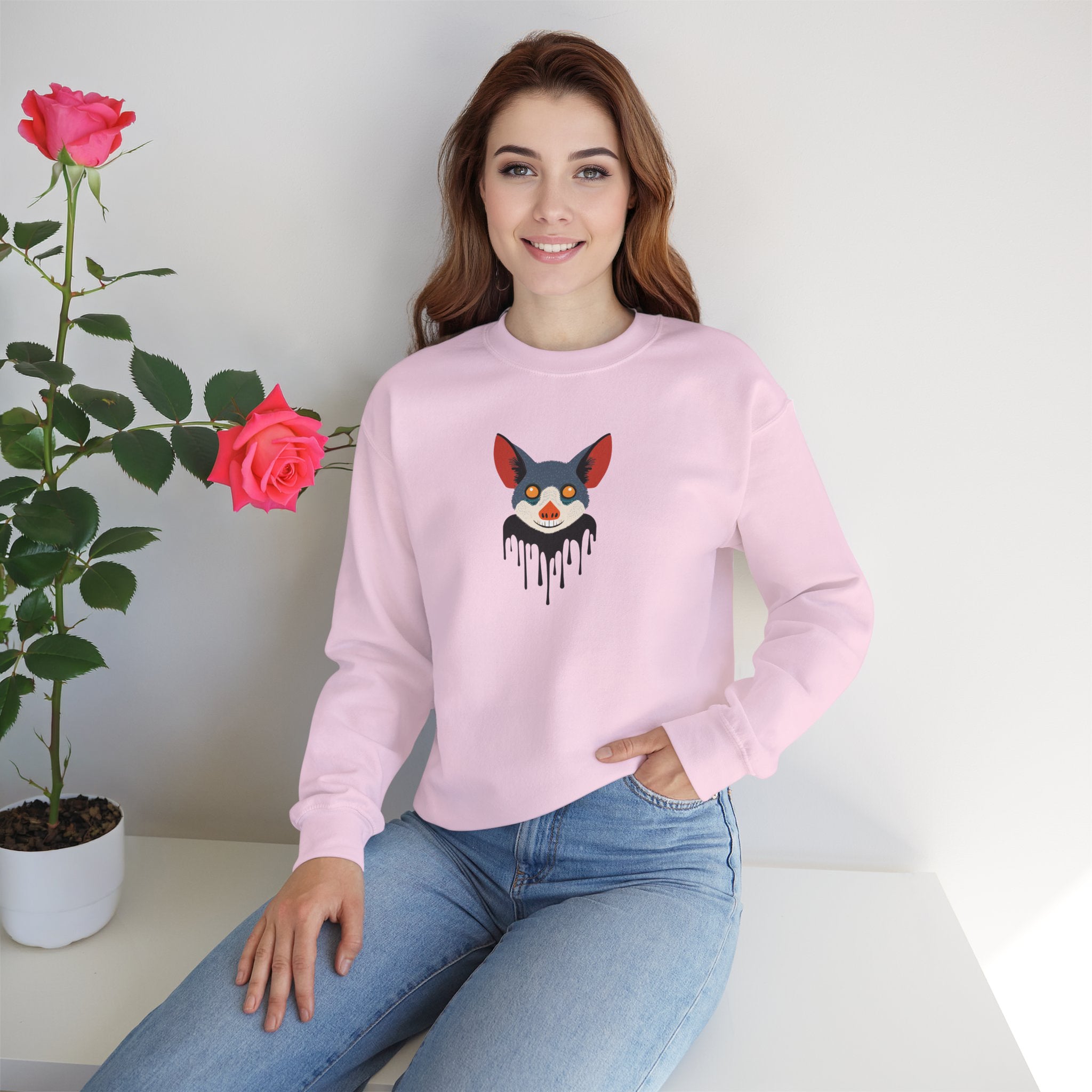 Woman wearing a pink sweatshirt with a graphic design, sitting next to a plant with red flowers.