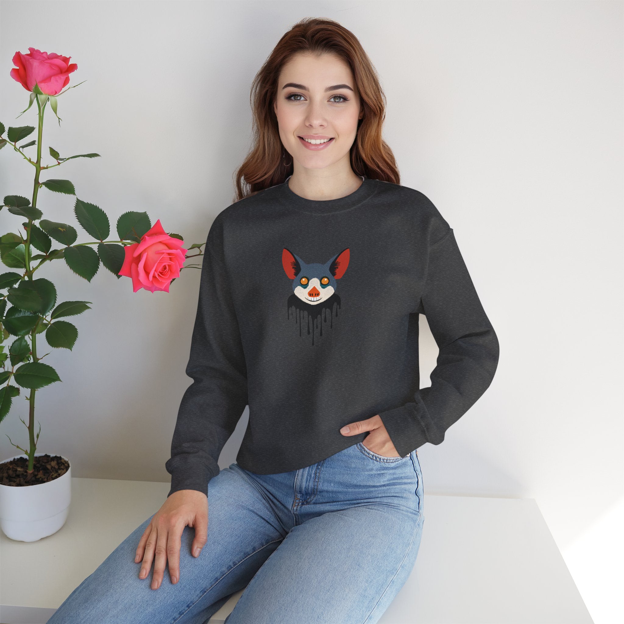 Woman wearing a black sweatshirt with a graphic design, sitting next to a potted plant with pink roses.