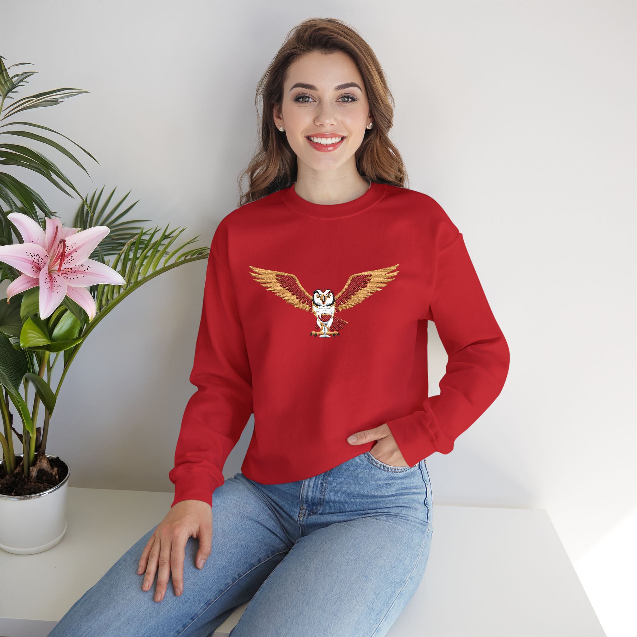 Woman wearing a red sweatshirt with an eagle design, sitting next to a potted plant.