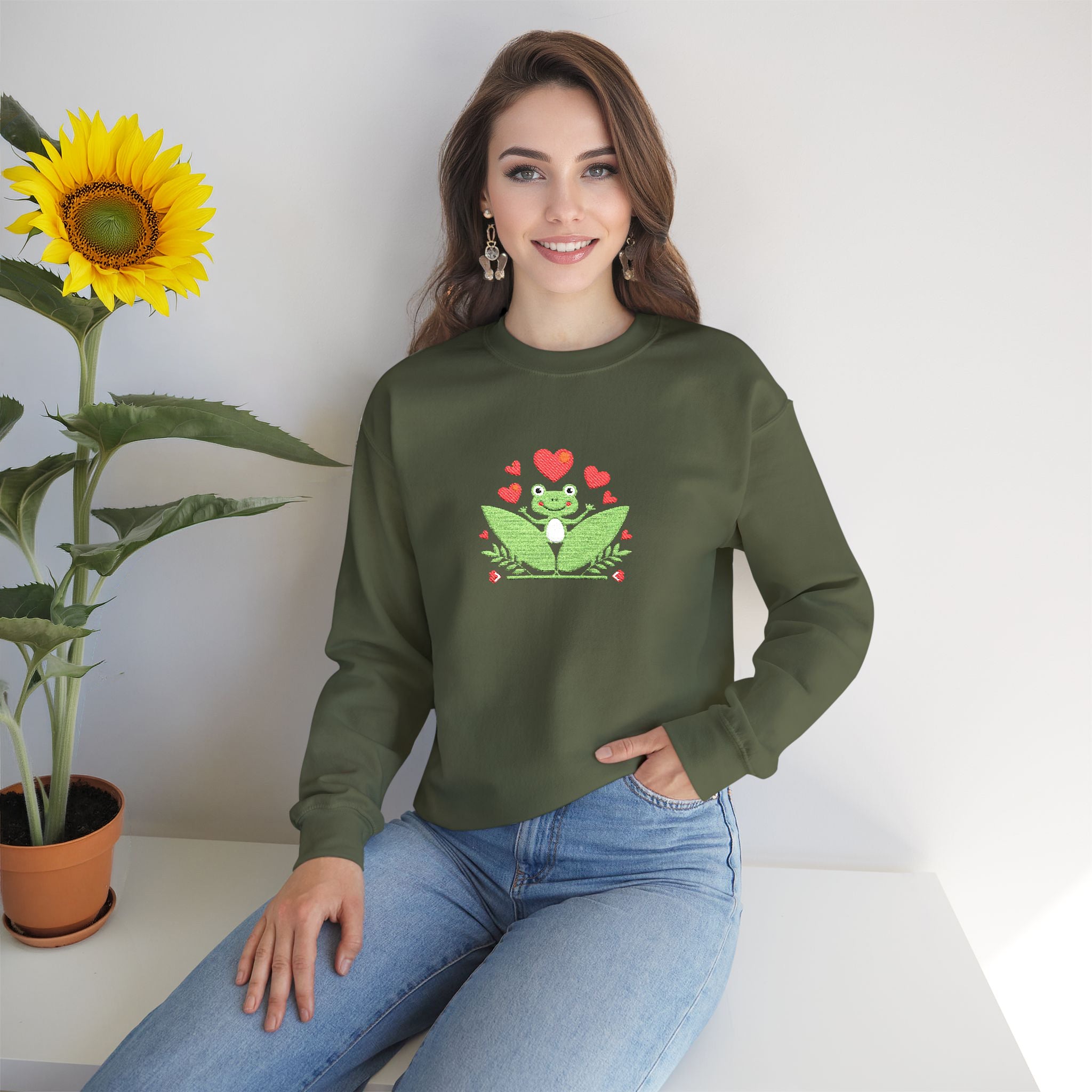 Woman wearing a green sweatshirt with a frog design, sitting next to a sunflower.