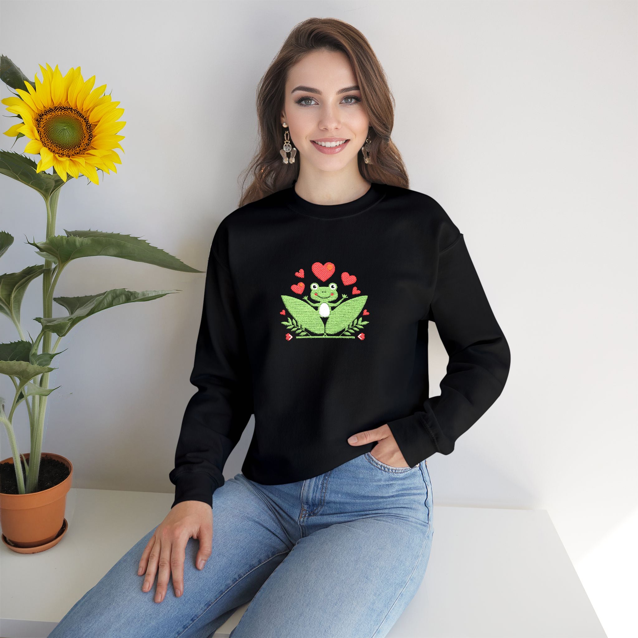 Woman wearing a black sweatshirt with a frog graphic sitting next to a sunflower.