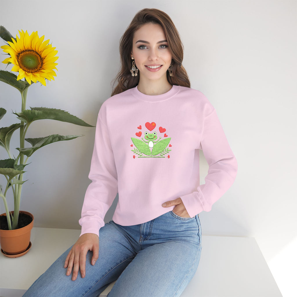 Woman wearing a pink sweatshirt with a frog design, sitting next to a sunflower.
