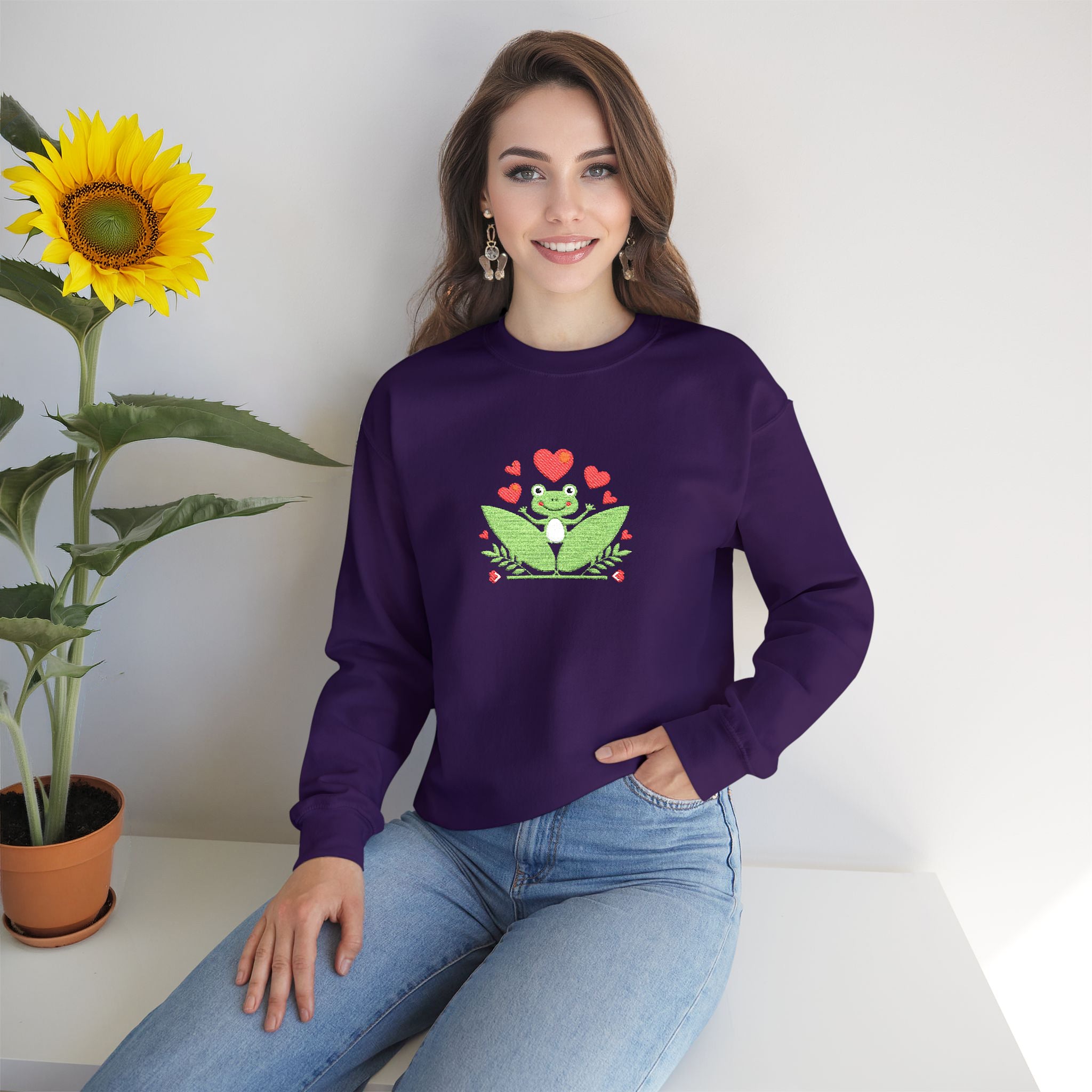 Woman wearing a purple sweatshirt with a frog design, sitting next to a sunflower.