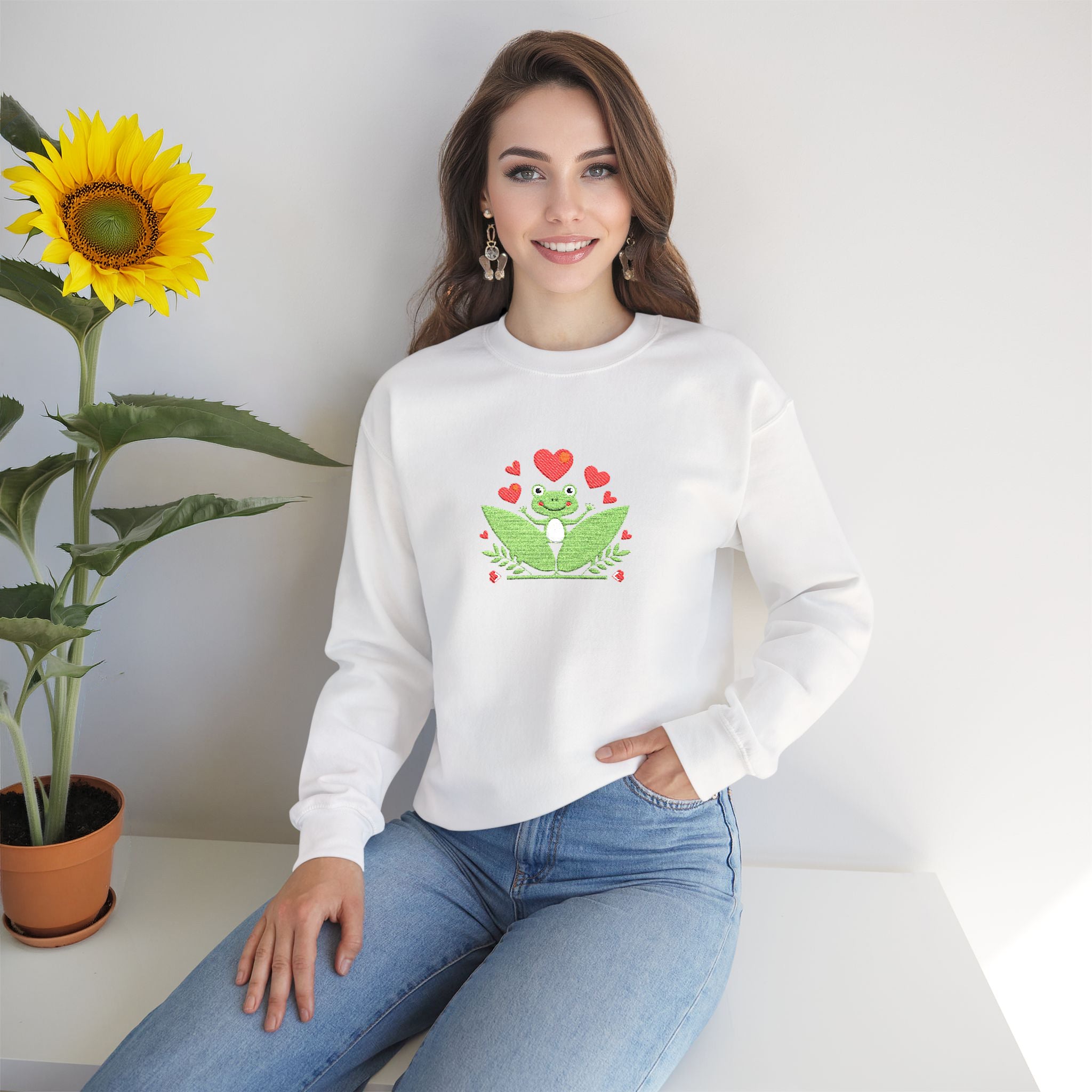 Woman wearing a white sweatshirt with a graphic design sitting next to a sunflower.