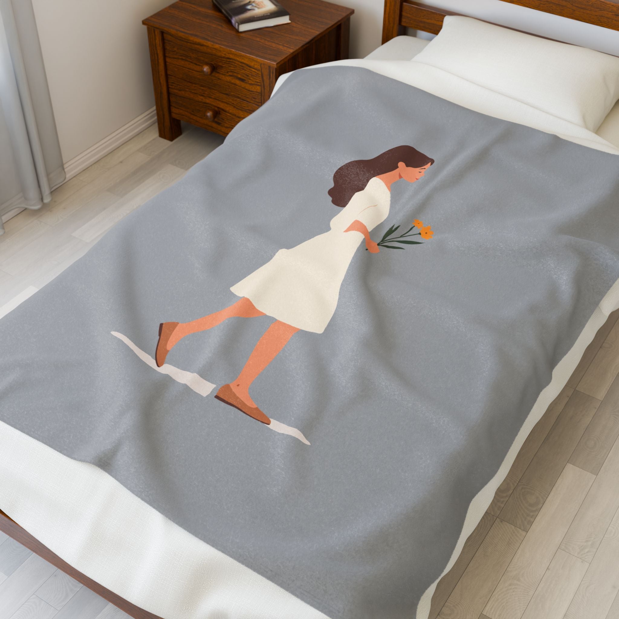 Gray blanket with a design of a woman holding flowers on a bed in a bedroom.