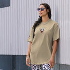 Woman wearing a light green t-shirt with a graphic design, standing against a textured wall.