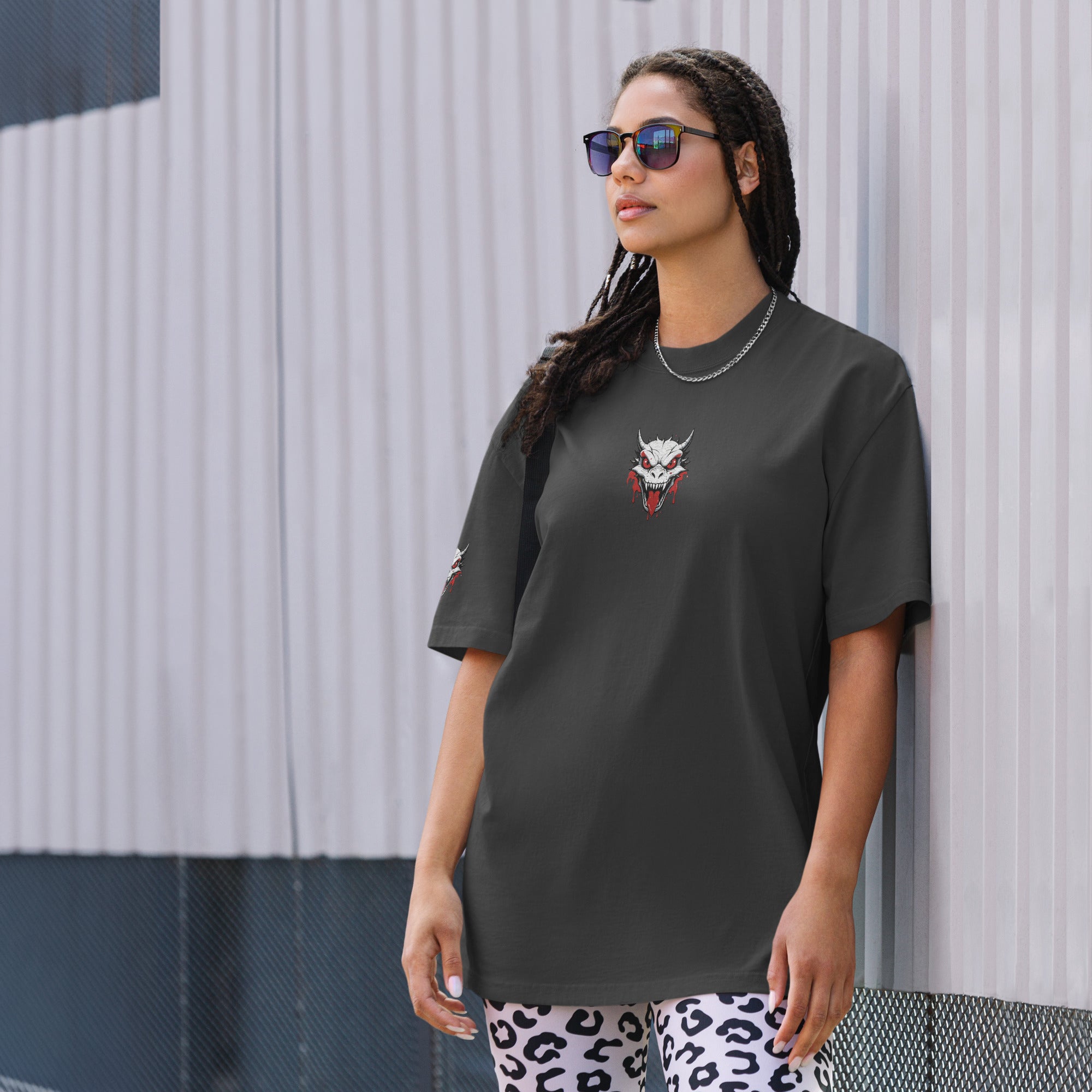 Woman wearing a dark gray t-shirt with a graphic design, standing against a textured wall.