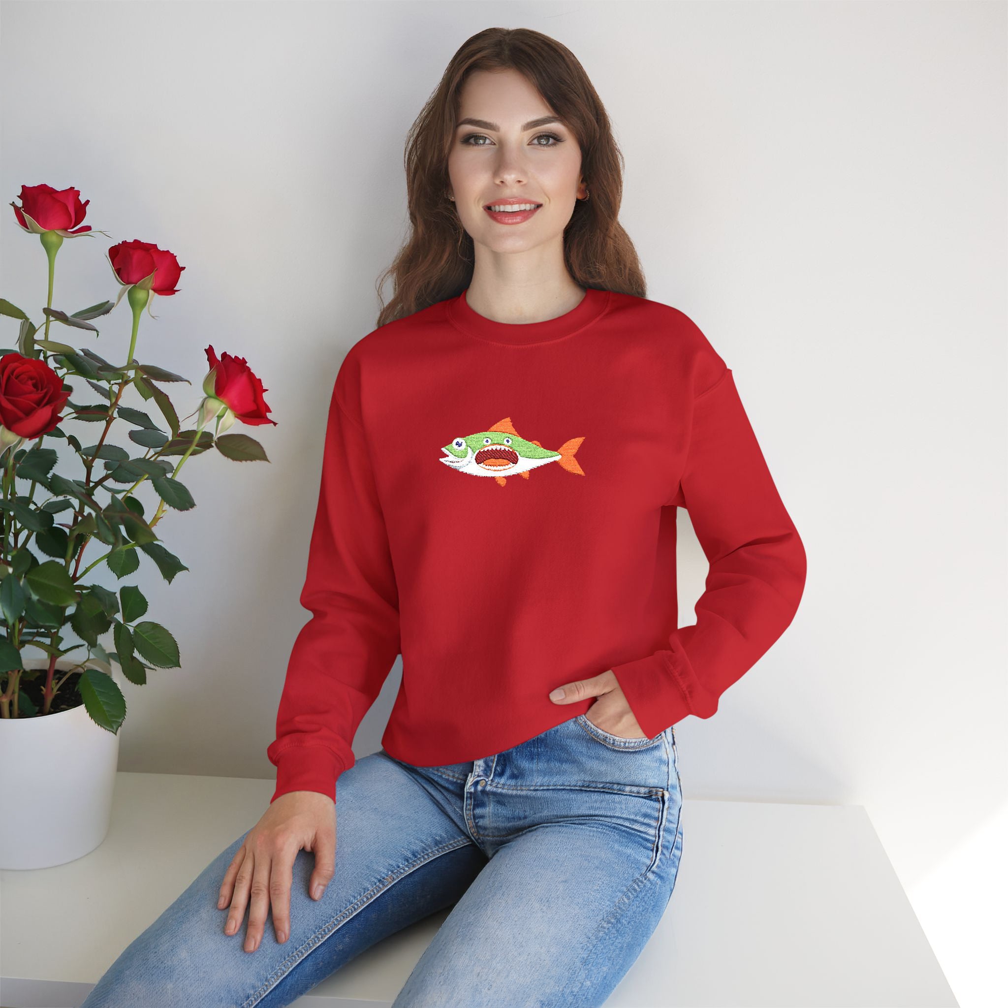 Woman wearing a red sweatshirt with a fish graphic, sitting next to a plant on a white surface.