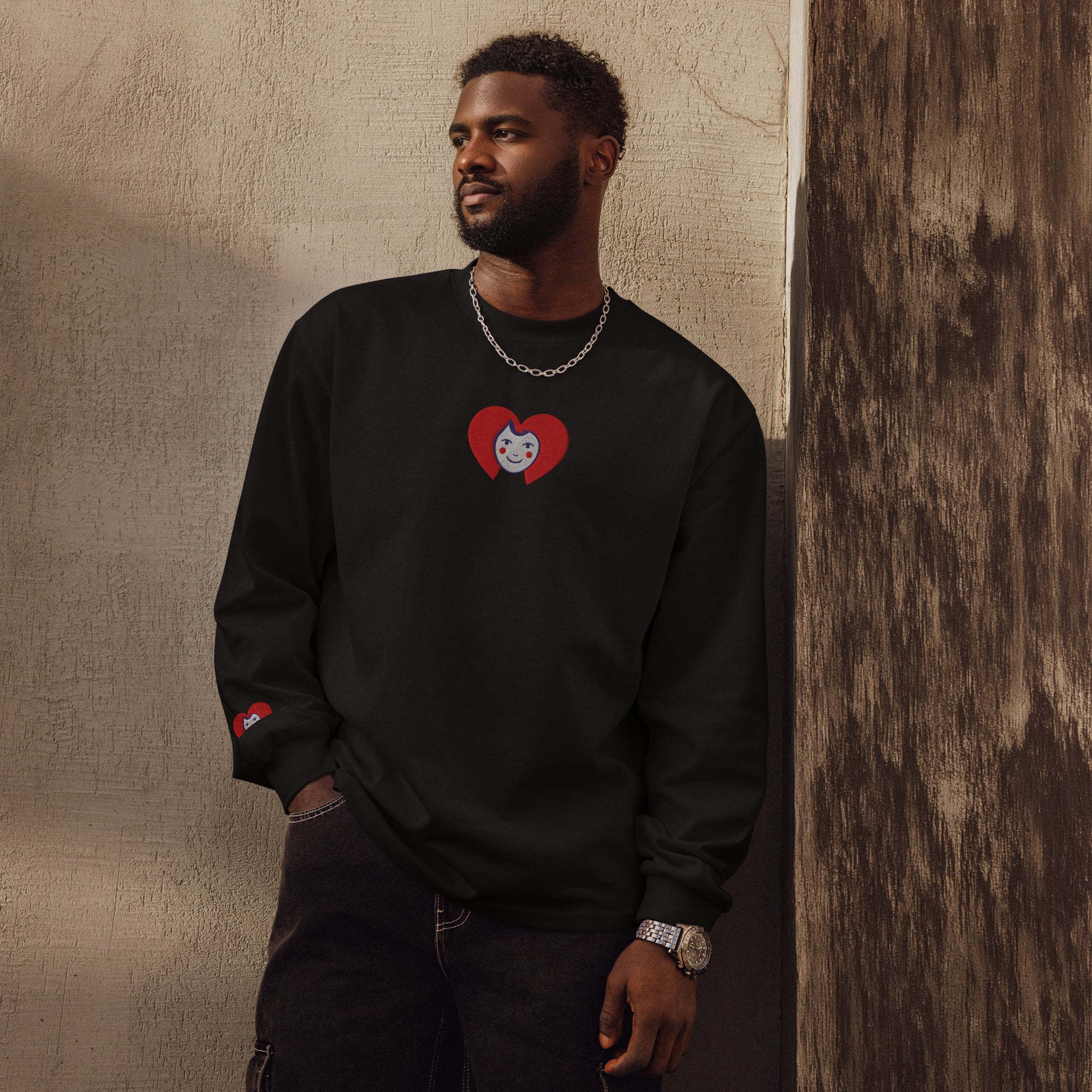 Man wearing a black sweatshirt with a red heart design, standing against a textured wall.
