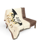 Blanket with bat design and text draped over a brown chair on a white background