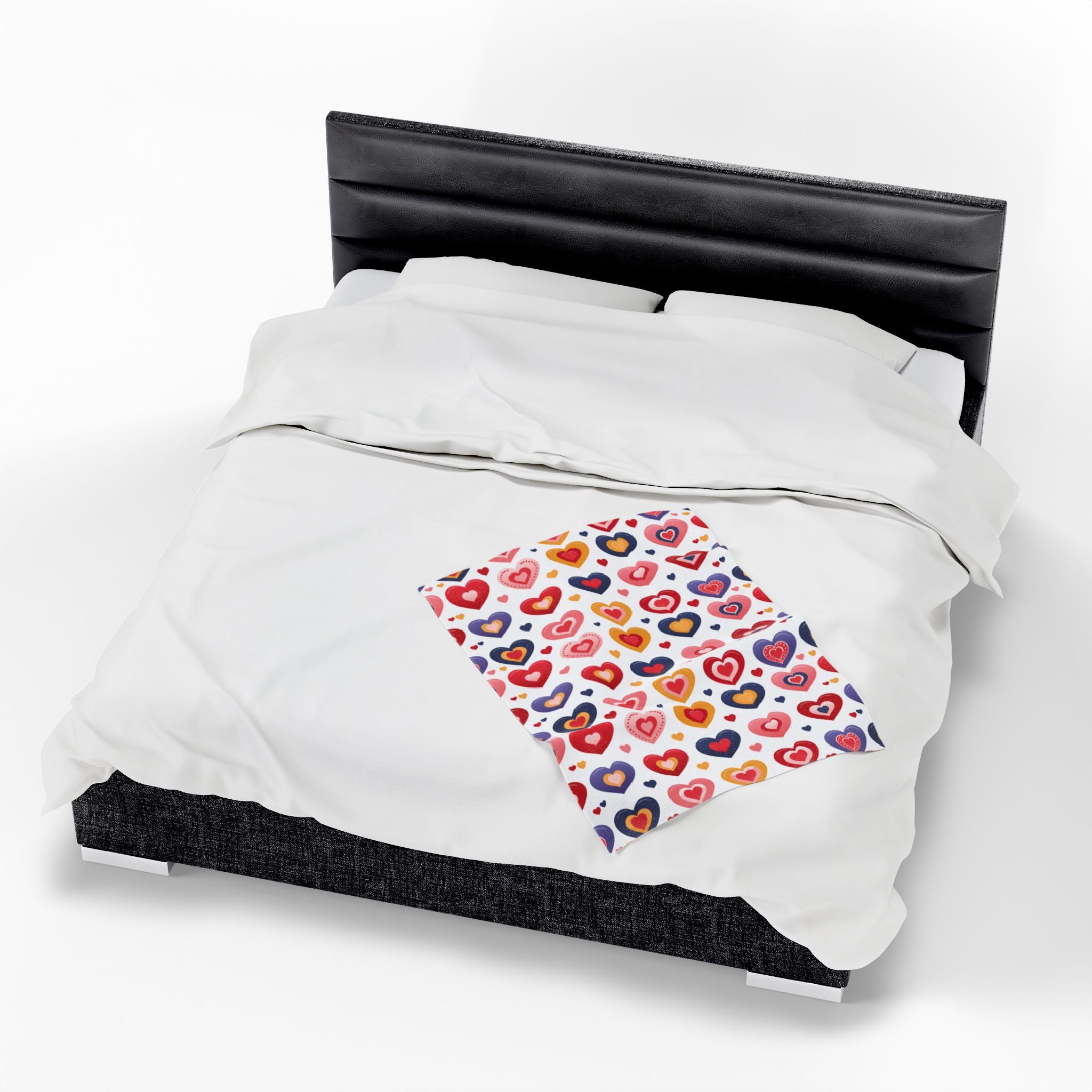 White comforter with a colorful heart-patterned pillow on a bed with black headboard.