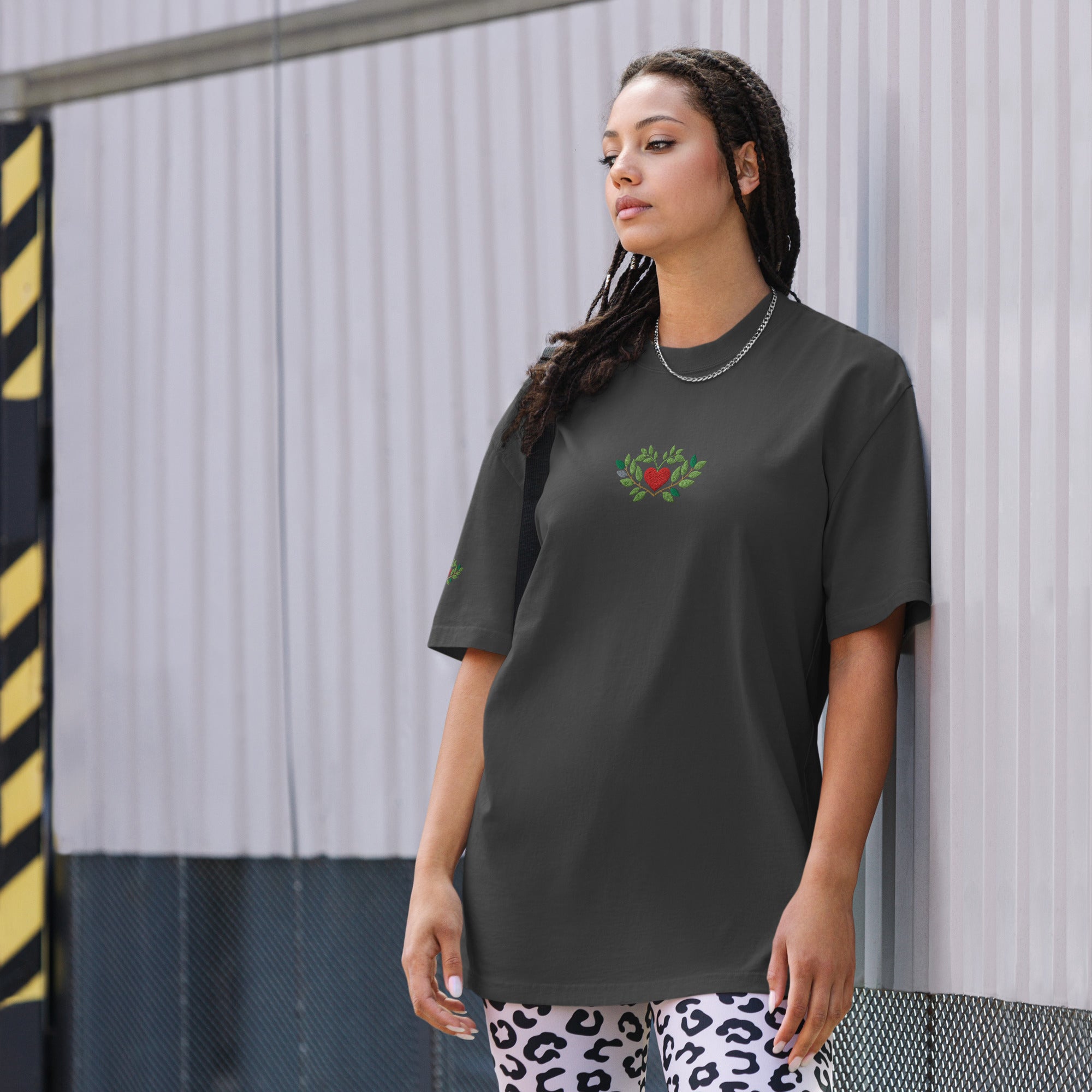 Woman wearing a dark gray t-shirt with a colorful design, standing against a metallic wall.