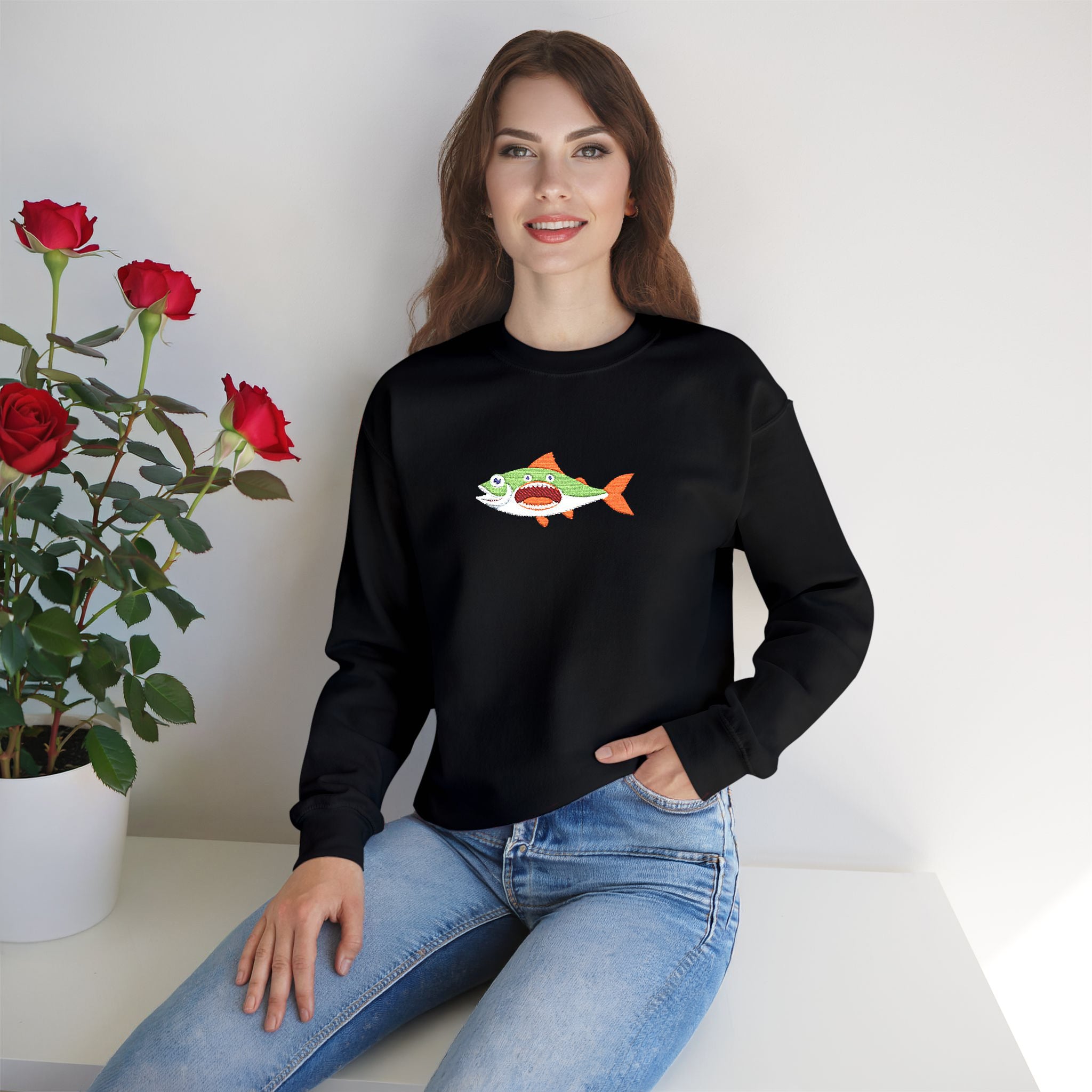 Woman wearing a black sweatshirt with a colorful fish design, sitting next to a potted plant with red flowers.
