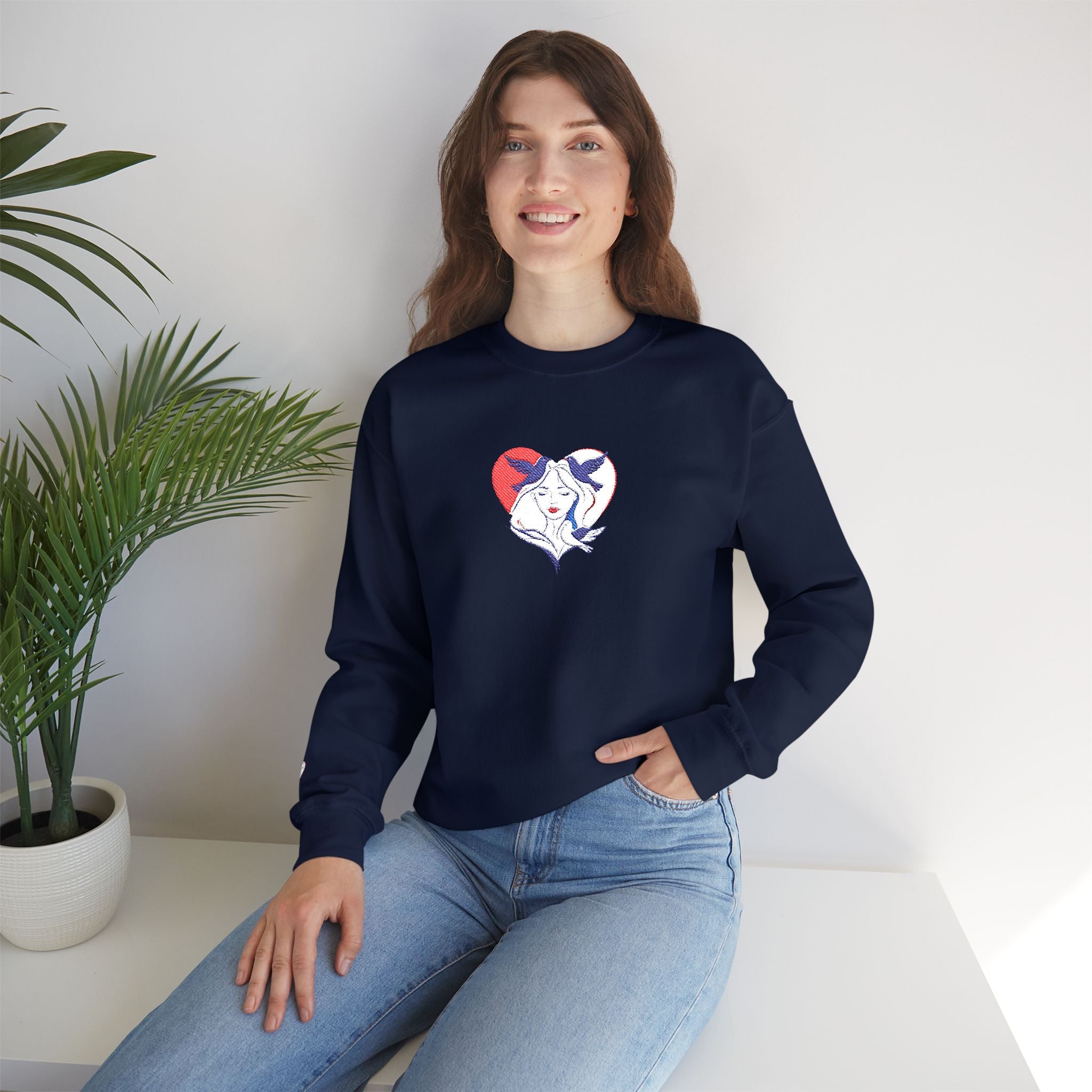 Woman wearing a navy blue sweatshirt with a heart design, sitting on a white surface with a plant in the background.
