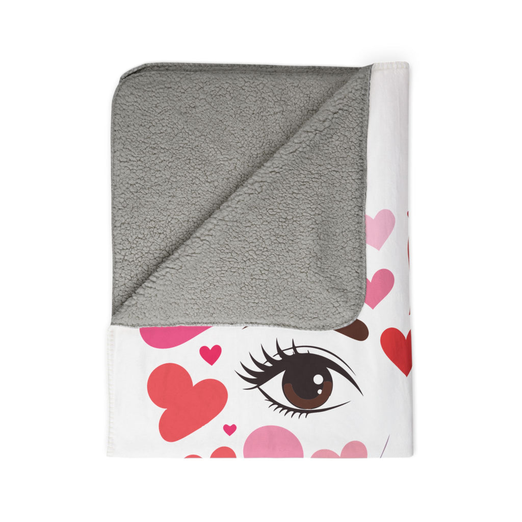 Folded blanket with gray hood and eye design featuring heart shapes on a white background