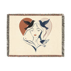 Woven blanket with a design of a woman's face, birds, and a heart on a beige background.
