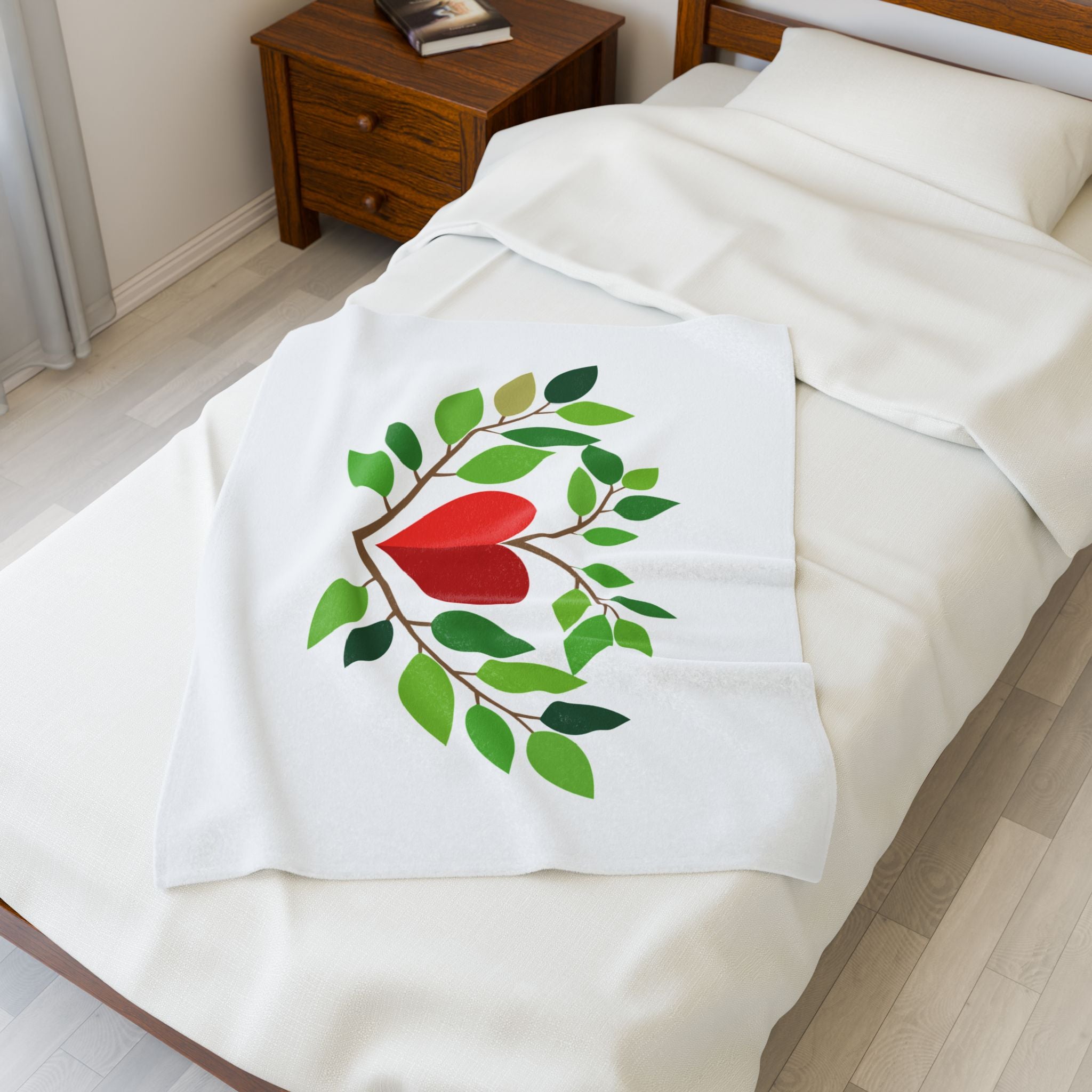 White blanket with a red heart and green leaves design on a bed.