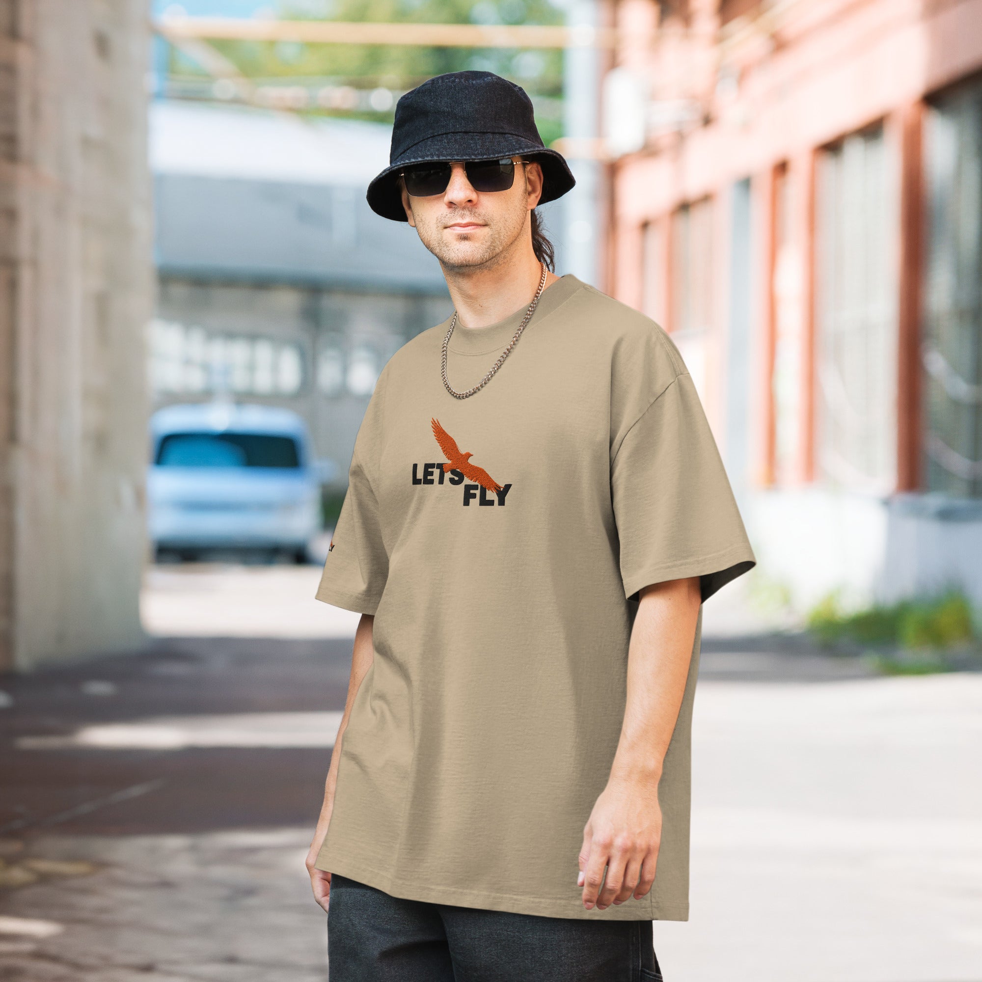 Man wearing a beige t-shirt with text and graphics, standing outdoors.