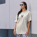 Woman wearing a white t-shirt with a graphic design, standing against a textured wall.