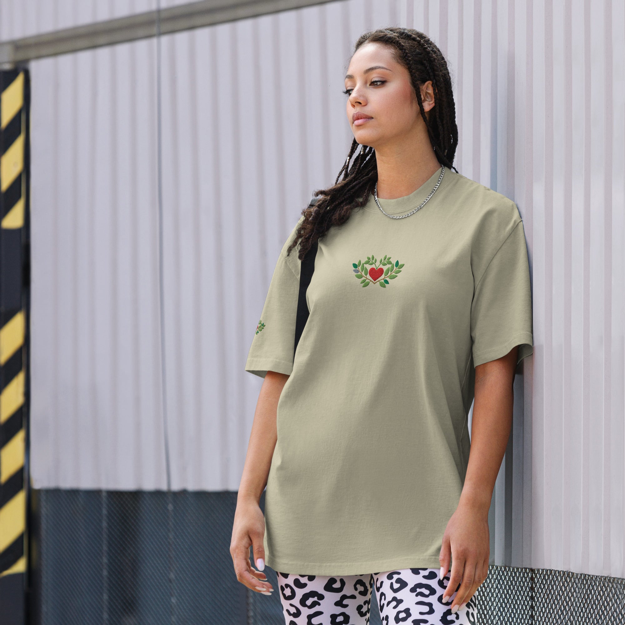 Woman wearing a light green t-shirt with a heart design against a metallic wall.