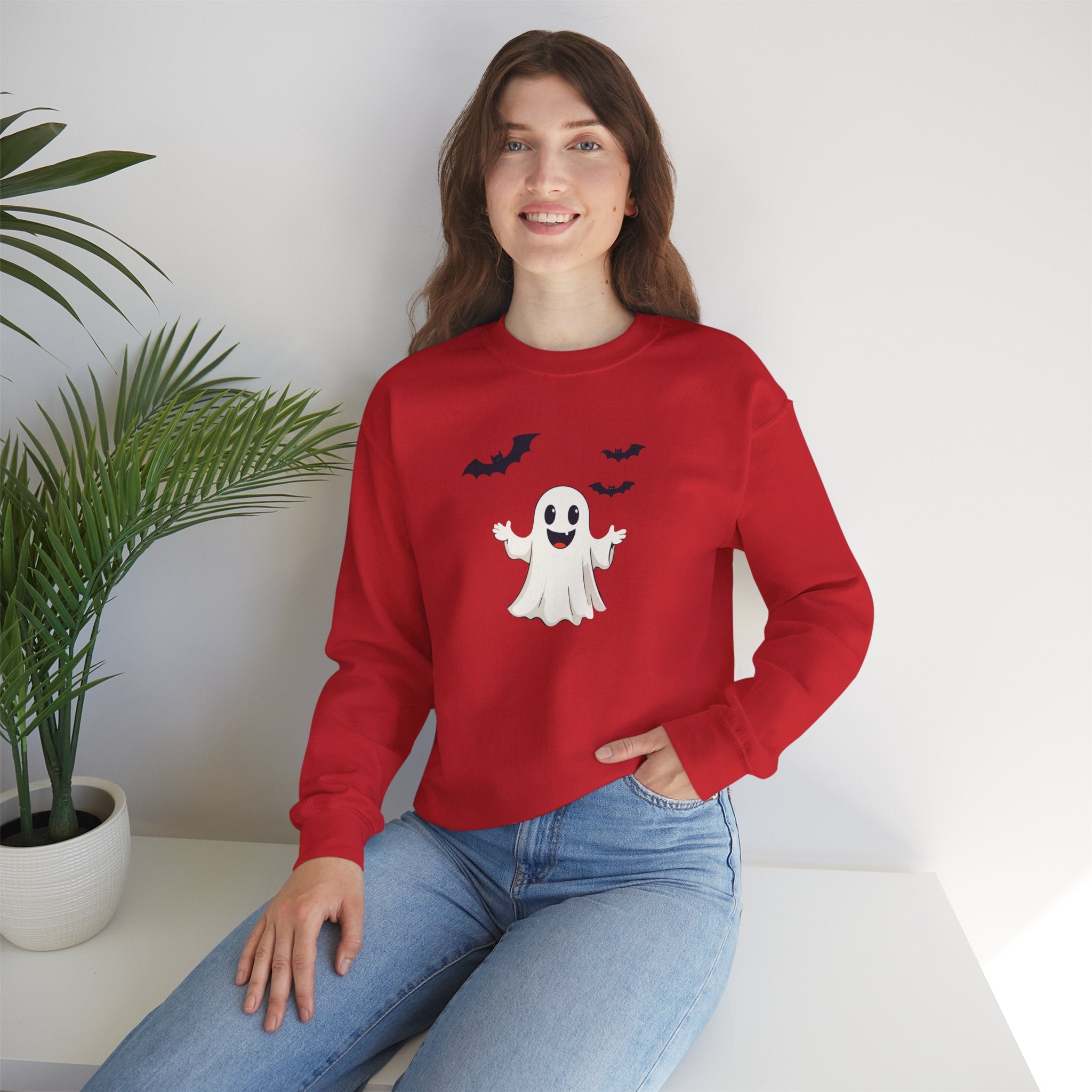Person wearing a red sweatshirt with a ghost design, sitting on a white surface with a plant in the background.