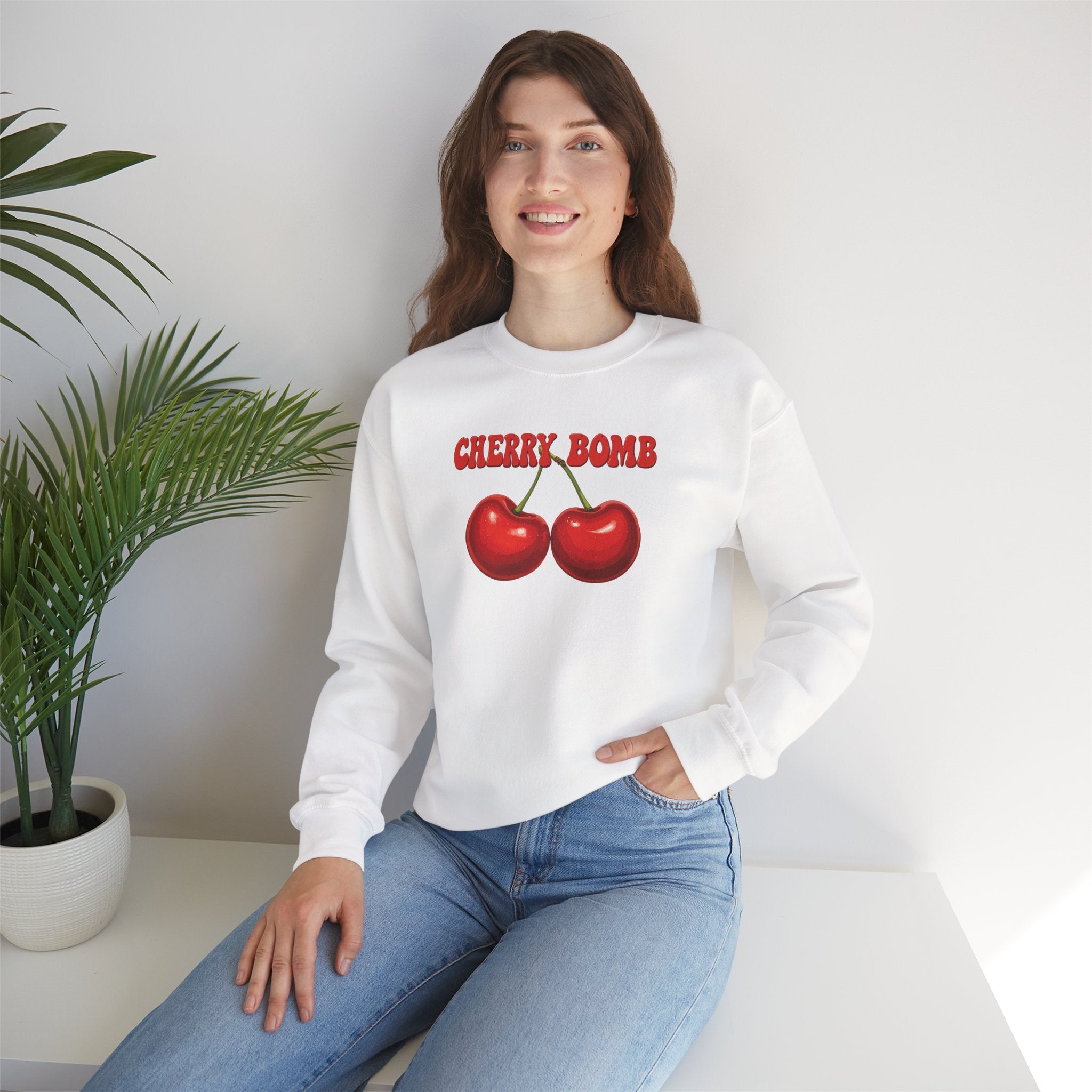 Woman wearing a white sweatshirt with 'Cherry Bomb' design sitting on a white couch.