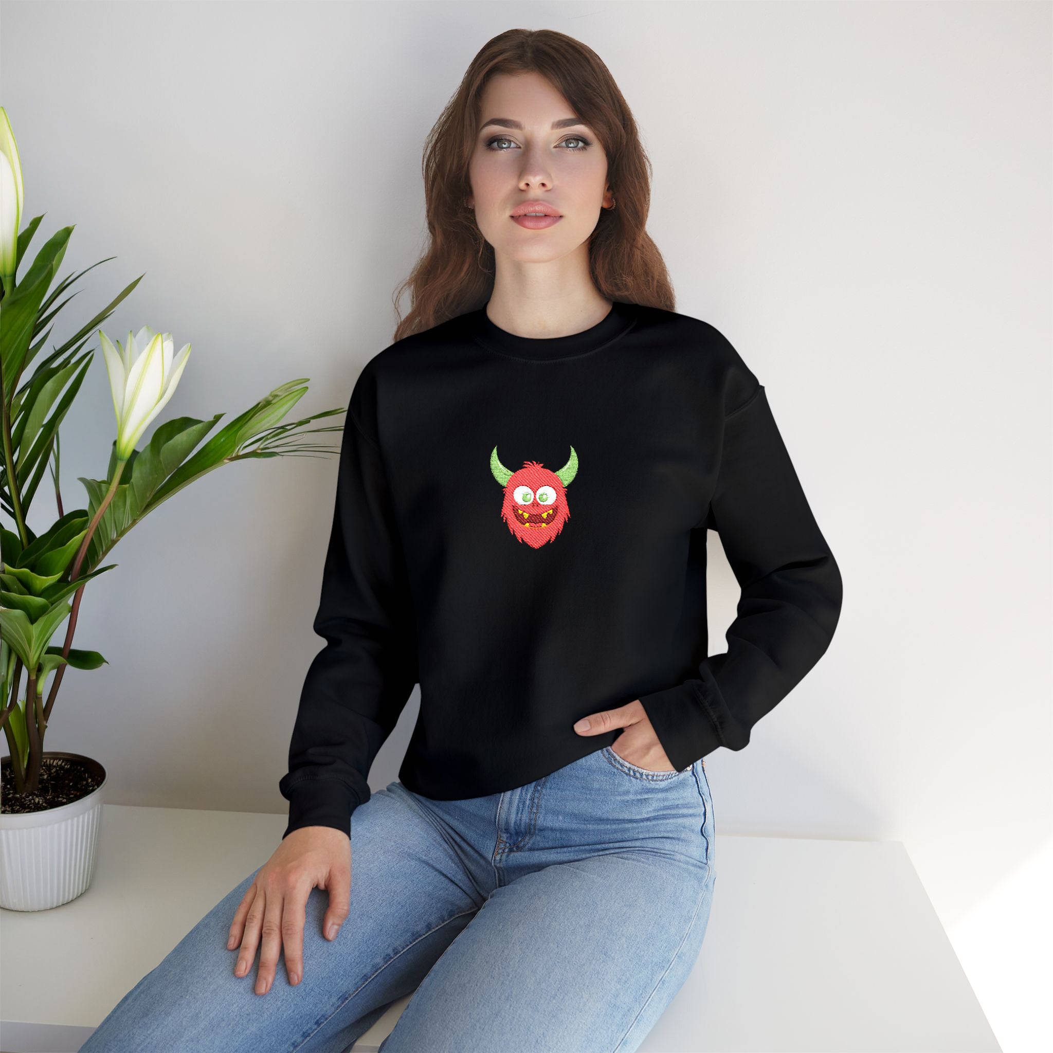 Woman wearing a black sweatshirt with a colorful graphic design sitting on a white surface with a plant in the background.
