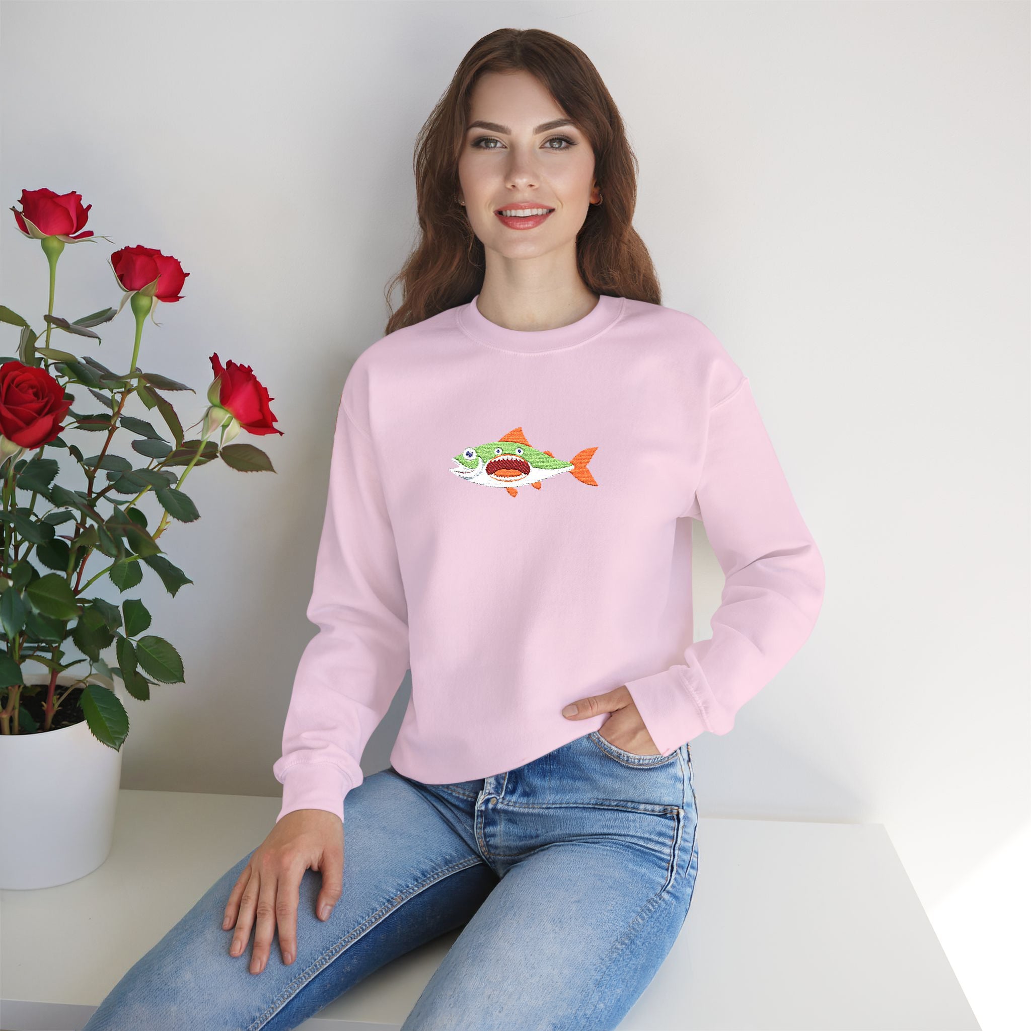 Woman wearing a pink sweatshirt with a fish design, sitting next to a potted plant with red roses.