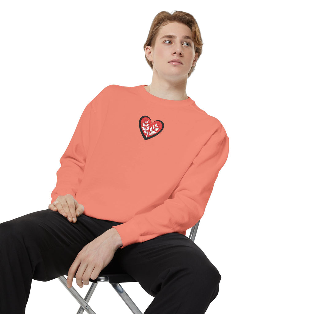 Person wearing a coral sweatshirt with a heart design sitting on a chair against a white background