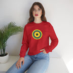 Woman wearing a red sweatshirt with a colorful emblem sitting on a white surface with a plant in the background.